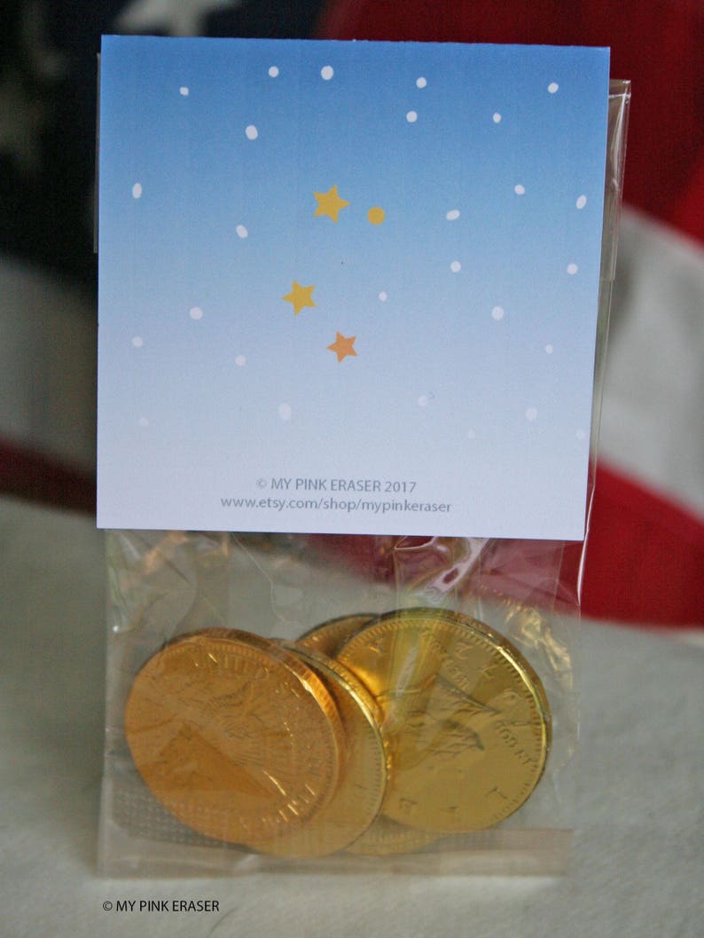 Puede incluir: Una bolsa de pl&aacute;stico transparente que contiene varias monedas de chocolate doradas. La bolsa est&aacute; sellada con una tarjeta que presenta un dise&ntilde;o de cielo azul degradado con puntos blancos y estrellas amarillas. El texto en la tarjeta dice "MY PINK ERASER 2017" y una direcci&oacute;n web.