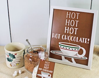 Puede incluir: Un cartel marrón enmarcado con letras blancas que dice "HOT HOT HOT HOT CHOCOLATE!" con una taza y un platillo blancos con hojas de acebo verdes y bayas rojas sobre un fondo marrón.