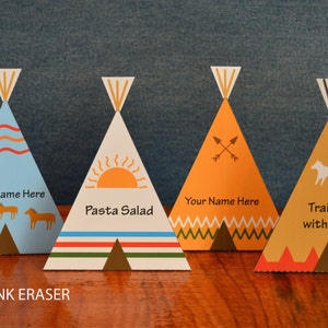 May include: Four colorful teepee-shaped paper place card holders with different designs. The first teepee is blue with a wavy design and the text "Your Name Here". The second teepee is white with a sun design and the text "Pasta Salad". The third teepee is orange with a cross-arrow design and the text "Your Name Here". The fourth teepee is yellow with a dog design and the text "Trail Mix with Nuts".