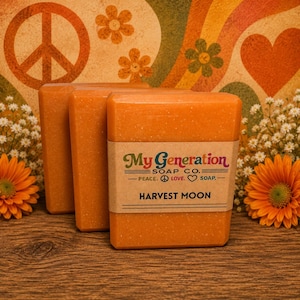 May include: Three rectangular bars of orange soap stacked together. A tan paper label wraps around the front bar with the text My Generation SOAP CO. PEACE. LOVE. SOAP. HARVEST MOON. The soap has a smooth texture and a vibrant orange color.