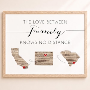 May include: A framed wall art print featuring the text THE LOVE BETWEEN Family KNOWS NO DISTANCE. Below the text are three wooden-textured state map silhouettes connected by a dotted line with small red hearts marking specific locations.