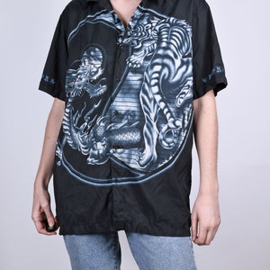 May include: Black short-sleeved button-up shirt with a white tiger and dragon yin-yang design.