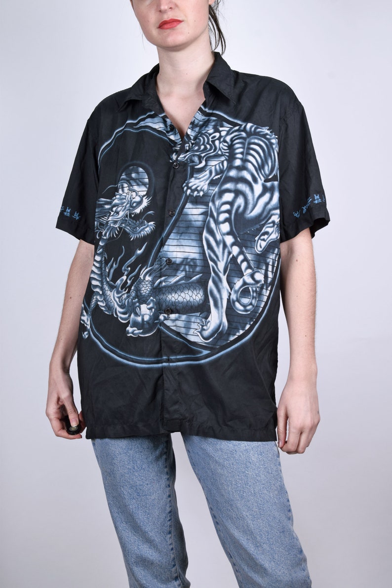 May include: Black short-sleeved button-up shirt with a white tiger and dragon yin-yang design.