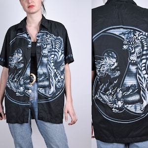 May include: Black button-up shirt with a white tiger and dragon design. The design is a yin-yang symbol with the tiger on one side and the dragon on the other.