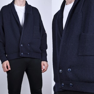 May include: A dark blue knitted cardigan with a shawl collar, two pockets, and a double-breasted button closure.