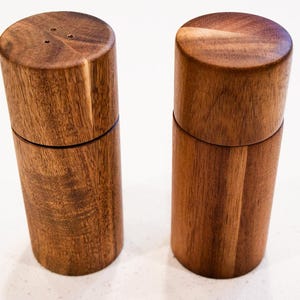 May include: Two wooden salt and pepper shakers with a natural wood finish. The shakers are cylindrical and have a simple design.
