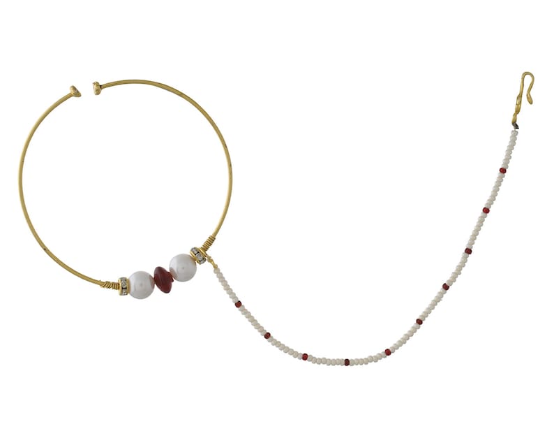 May include: A gold-toned nose ring with a large circular design. The ring features white and red beads, and a delicate chain of white beads with red accents. The design includes a hook for secure placement.