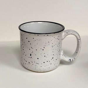 May include: White ceramic mug with a black speckled design and a black rim.