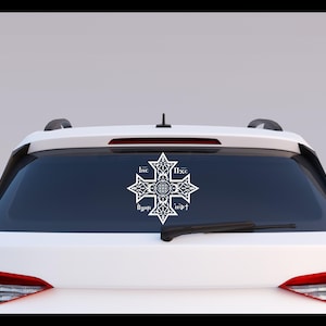 May include: White vinyl decal of a stylized cross with the text "IHC" and "NIKA" in a circular design. The decal is applied to the rear window of a white car.