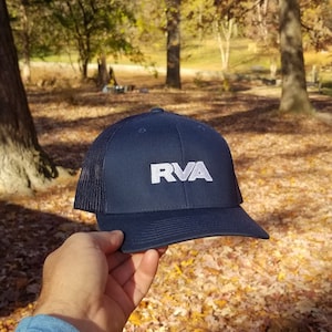 May include: A navy blue trucker hat with a white mesh back and a white embroidered logo that says "RVA".