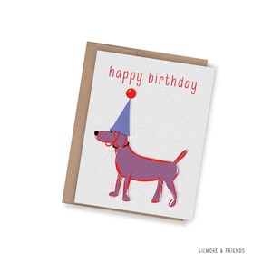May include: A birthday card with a red and blue patterned dog wearing a party hat. The words "happy birthday" are written in red. The card is on a brown envelope.
