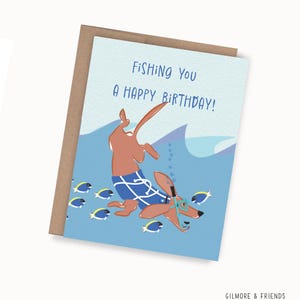 May include: A birthday card featuring a cartoon dachshund wearing swim goggles and blue swim trunks, diving underwater. The card reads "Fishing You A Happy Birthday!" with blue waves and fish illustrations.