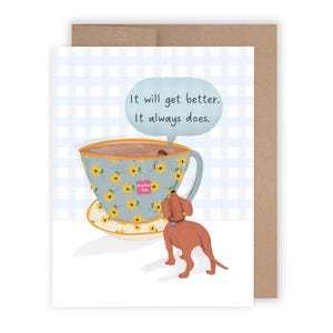 May include: Greeting card featuring a whimsical illustration. A large teacup with a floral pattern and a tea bag labeled "Positive Tea" is depicted. A brown dog stands near the cup. The text "It will get better. It always does." is in a speech bubble.