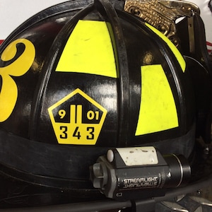 May include: Black firefighter helmet with yellow reflective markings. The helmet has a number "9 01 343" on the front and a Streamlight flashlight attached to the side.
