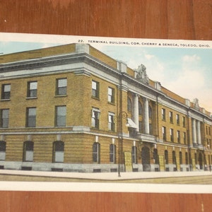 May include: Vintage postcard featuring the Terminal Building in Toledo, Ohio. The building is a multi-story structure with a yellow brick facade, white columns, and a flat roof. The postcard has the text "22. TERMINAL BUILDING, COR. CHERRY & SENECA, TOLEDO, OHIO."