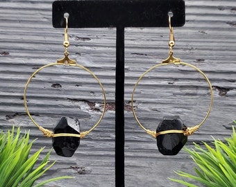 May include: Gold hoop earrings with a black gemstone dangling from each hoop.