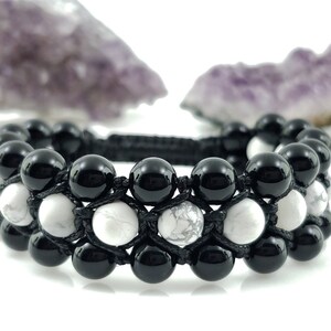 May include: Black and white beaded bracelet with black cord. The bracelet has two rows of beads, one row of black onyx beads and one row of white howlite beads.
