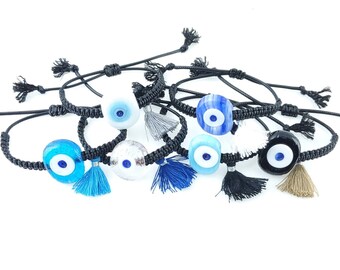May include: A set of seven black string bracelets with blue evil eye charms and colorful tassels. The charms are made of glass and have a white center with a blue eye.