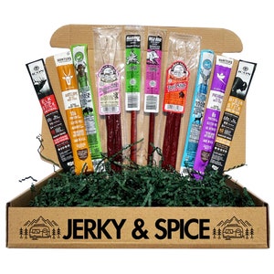 May include: A brown cardboard box with the words "JERKY & SPICE" printed on the front. The box is filled with green shredded paper and contains eight different flavors of meat sticks. The meat sticks are individually wrapped in clear plastic and labeled with the flavor and nutritional information.