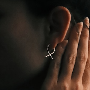 Puede incluir: Una mujer con el pelo oscuro lleva una blusa marrón y un pendiente de plata en forma de ocho.