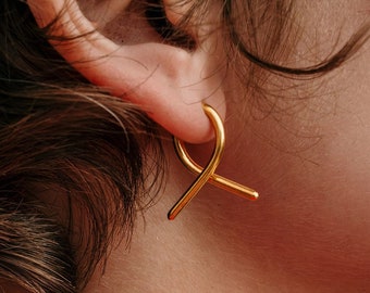 May include: A person wearing a red shirt with gold hoop earrings. The earrings are shaped like a figure eight.