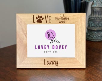 May include: A light wooden picture frame with the text "LOVE" and a paw print, and "is a four-legged word". The frame has a white insert with a bird graphic and the words "LOVEY DOVEY GIFT CO." and the name "Lanny".