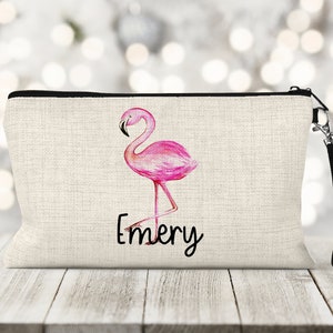May include: A pink flamingo design on a beige canvas zippered pouch with a black strap. The pouch has the name "Emery" printed on it.