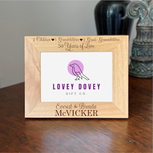 May include: A light-colored wooden picture frame with the text "2 Children 5 Grandchildren 2 Great-Grandchildren 50 Years of Love." The frame features a logo with a bird and the words "LOVEY DOVEY GIFT CO." and the names "Everest & Brenda McVICKER."