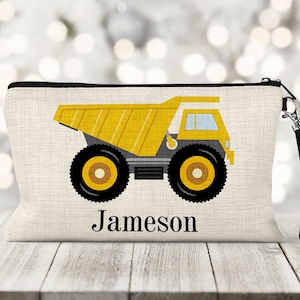 May include: A yellow and black dump truck with a personalized name "Jameson" printed on a beige canvas zippered pouch with a black strap.