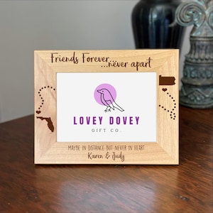 May include: A light-colored wooden picture frame with the text "Friends Forever...never apart." The frame features a logo with a bird and the words "LOVEY DOVEY GIFT CO." The frame also includes the text "MAYBE IN DISTANCE BUT NEVER IN HEART Karen & Judy."
