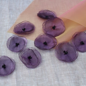 May include: Purple fabric flowers with black centres. The flowers are layered and have a delicate, ruffled appearance.