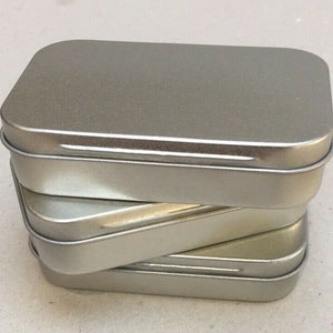 May include: Three silver metal rectangular boxes stacked on top of each other. The boxes are empty and have a smooth, shiny surface.