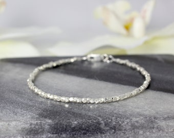 May include: A delicate silver bracelet composed of numerous small, faceted, metallic beads strung together in a continuous circular chain, featuring a small, polished silver clasp mechanism at the back for secure fastening.