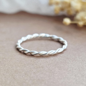 May include: A thin, circular ring crafted from polished silver metal. The band features a continuous twisted rope design, creating a textured appearance around the entire circumference of the jewellery piece, which is shown in a clear, focused view.