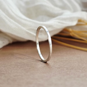 May include: A thin, silver-coloured ring with a hammered, textured surface. The band has a circular shape and a reflective metallic finish, standing upright on its edge to showcase the subtle indentations along the outer circumference of the metal.