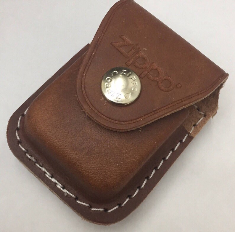 May include: A brown leather Zippo lighter case with a snap closure. The case has white stitching around the edges and the Zippo logo is embossed on the flap. The snap is silver and has the Zippo logo.