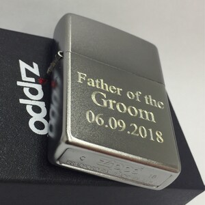 May include: A silver Zippo lighter with the inscription "Father of the Groom 06.09.2018" engraved on the front. The lighter rests on a black box with the Zippo logo. A classic gift.