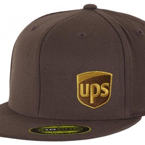 May include: A brown baseball cap with a flat brim. The cap features the UPS logo embroidered on the front in gold and brown. The hat is a fitted style.