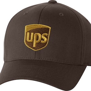 May include: A brown baseball cap featuring the UPS logo embroidered on the front. The logo is a gold shield with the letters "ups" in gold. The cap is made of a durable fabric and has a curved brim.