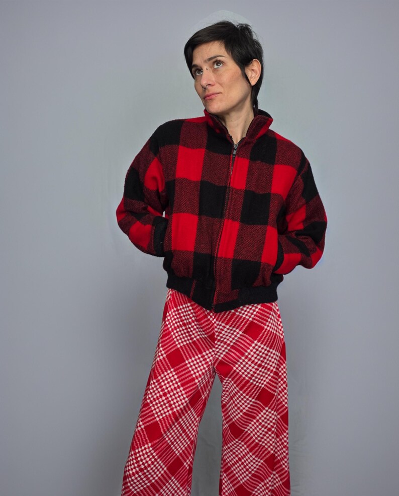 A woman wearing a red and black plaid jacket and red and white plaid pants stands against a gray background.