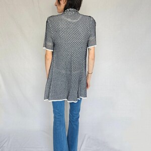 May include: A black and white patterned tunic with short sleeves and a white trim. The tunic is worn over blue jeans.