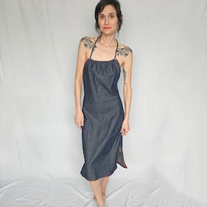 May include: A dark blue denim dress with a halter neckline and a side slit. The dress is midi length and has a relaxed fit.