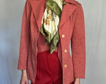 May include: A vintage red blazer with a small check pattern, paired with matching red pants. A patterned scarf in shades of green, cream, and yellow is worn with the blazer. The blazer has three wooden buttons.