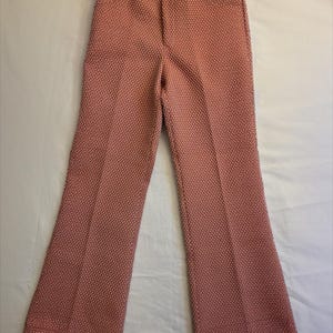 May include: Pink and white patterned trousers with a high waist and flared legs. The trousers have a textured fabric and a button closure. The trousers are a vintage style.