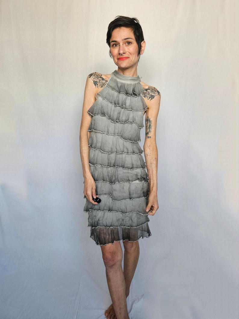 a woman in a gray dress standing in front of a white backdrop