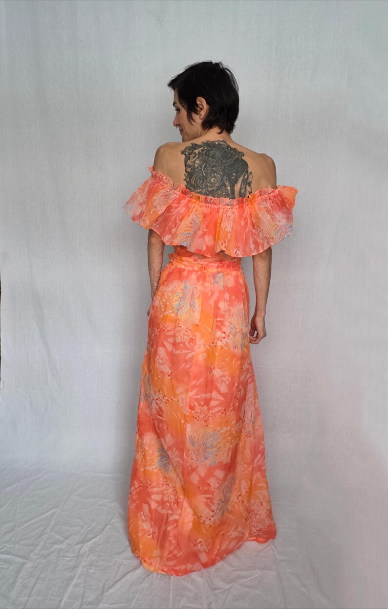 A woman wearing a vibrant, floral-patterned dress with off-the-shoulder sleeves stands against a plain white background.