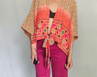 Pode incluir: Uma vibrante parte superior estilo quimono com frente aberta e um padrão geométrico colorido em tons de laranja, amarelo e rosa. A parte superior é combinada com calças rosa brilhante. A roupa é uma declaração de moda ousada.