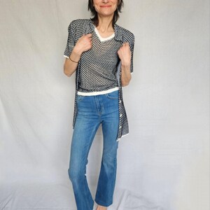 May include: A woman wearing a white and black patterned shirt over a white mesh top and blue jeans.