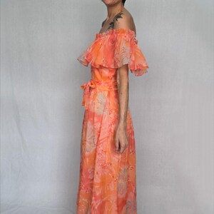 A woman wearing a long, off-the-shoulder dress with a floral print stands against a white background.