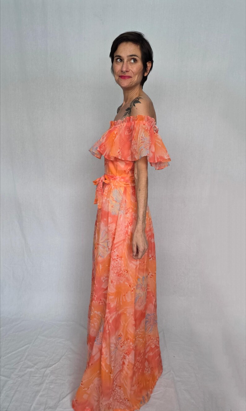A woman wearing a long, off-the-shoulder dress with a floral print stands against a white background.